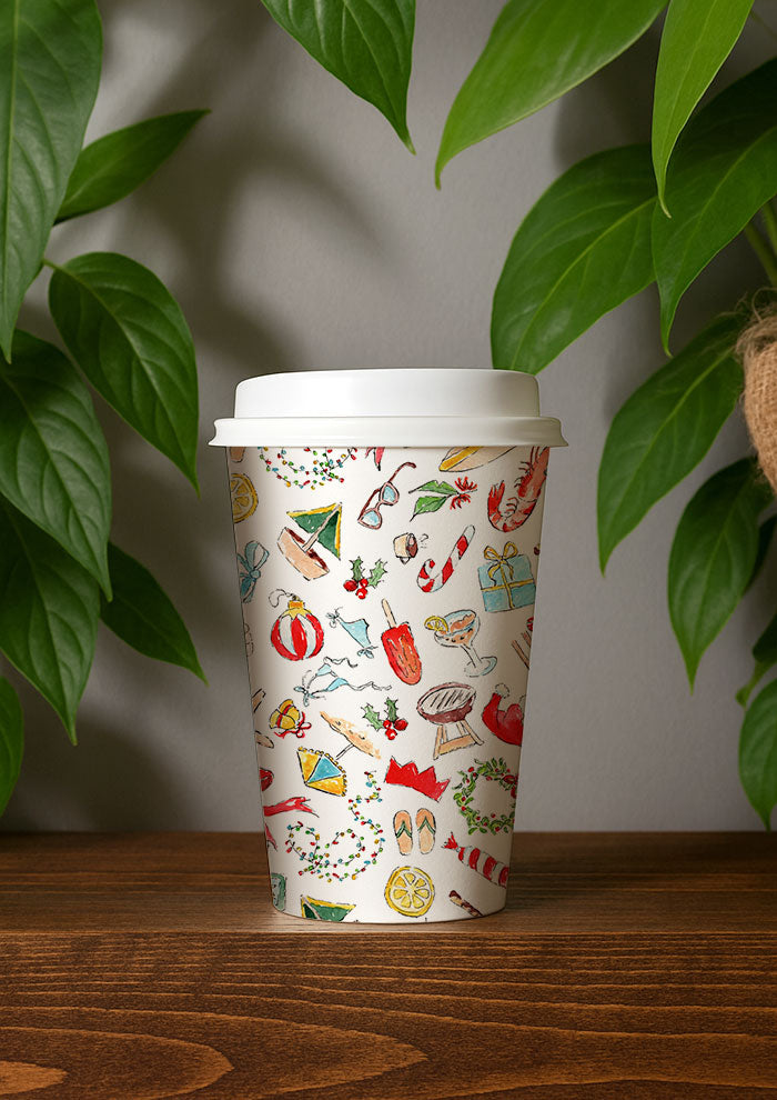 Paper Coffee cup with colorful Christmas design on a wooden surface with green leaves in the background by Australian Surface Pattern Designer Laura Hamzic
