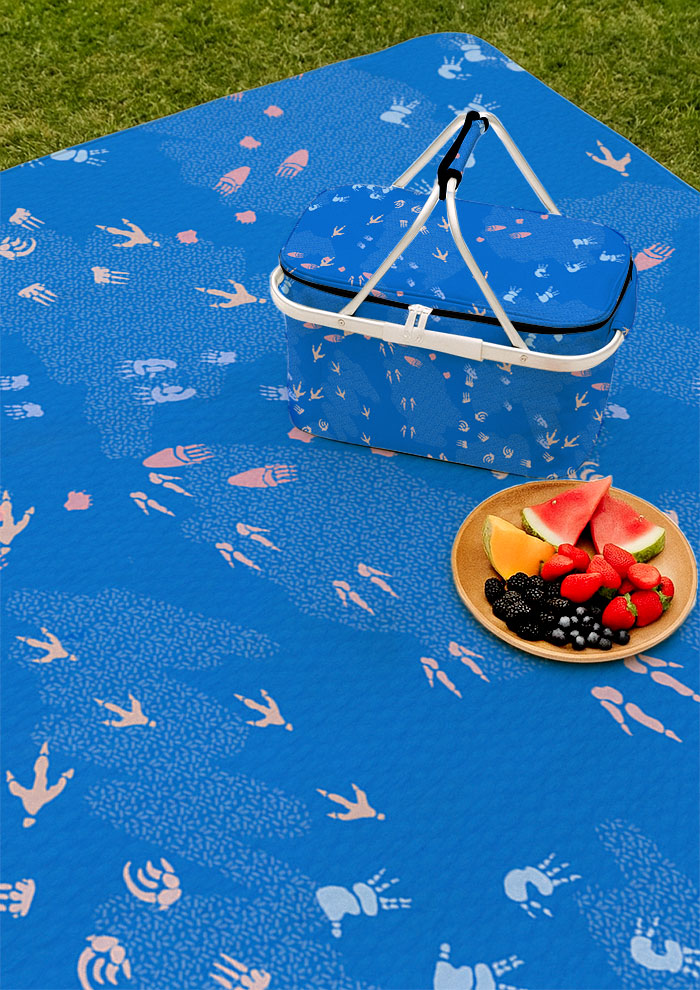 Blue picnic blanket and picnic featuring whimsical Australian wildlife footprints – kangaroo, echidna, wombat, and more – inspired by bushland trails and nature’s stories. Surface pattern design Australia.