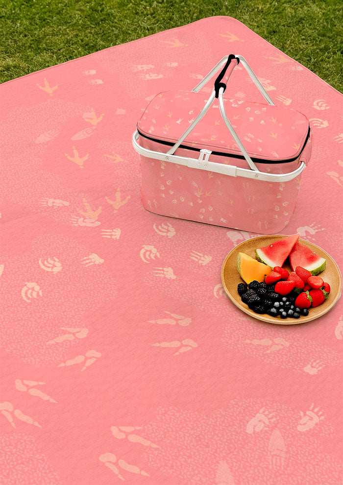 Pink picnic blanket and picnic featuring whimsical Australian wildlife footprints – kangaroo, echidna, wombat, and more – inspired by bushland trails and nature’s stories. Surface pattern design Australia.