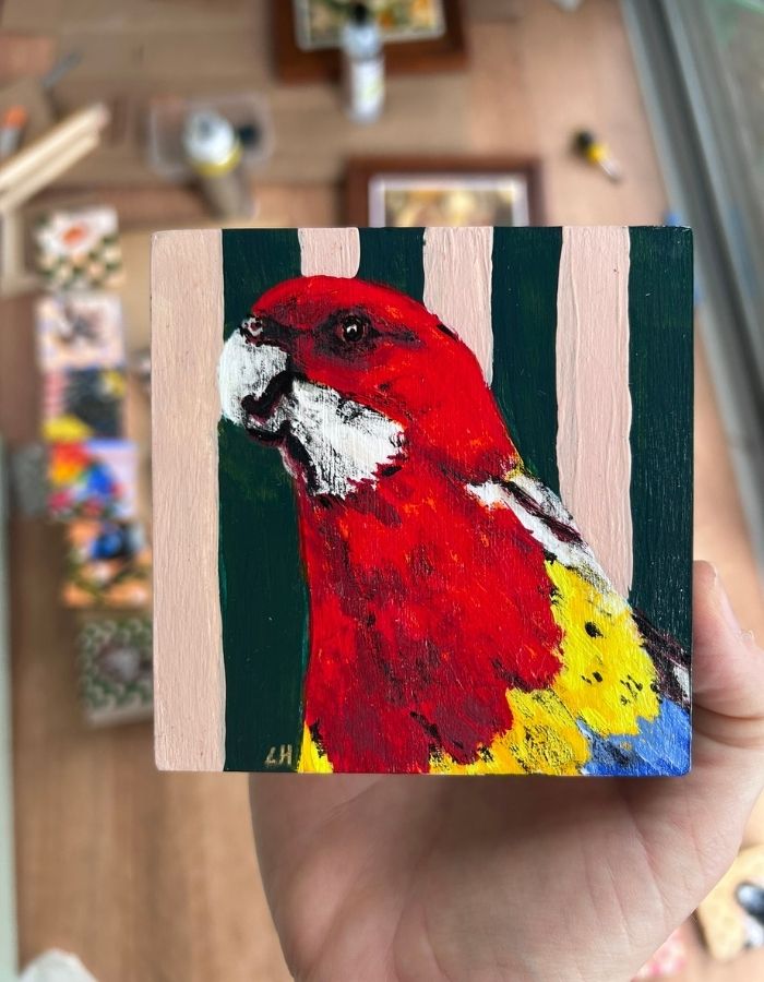 Original 10 × 10 cm eastern rosella painting held in hand