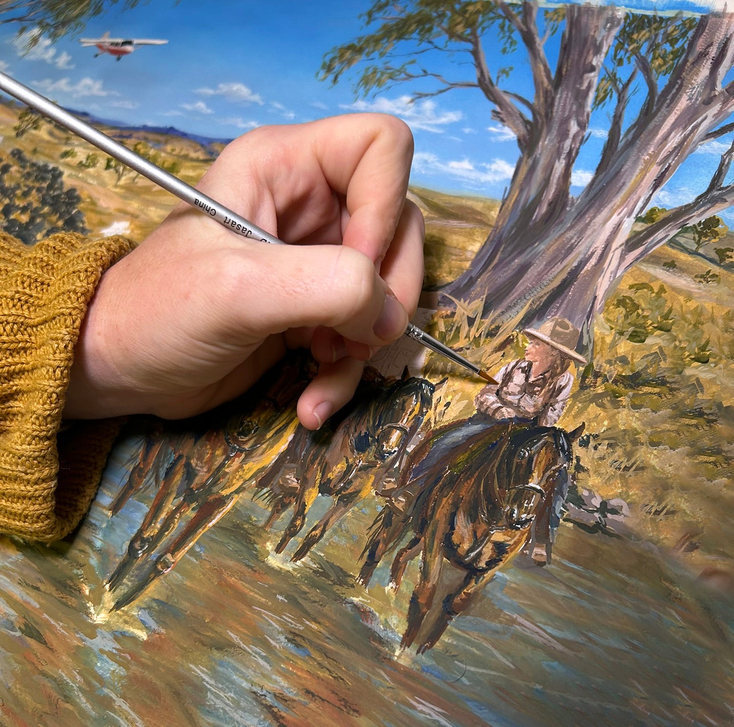 Hand painting a scene of a person on horseback with a landscape in the background.