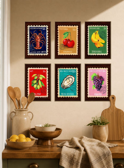Six framed colorful art prints depicting seafood and fruit illustrations are arranged in a 2x3 grid on a beige wall above a wooden kitchen counter with bowls, lemons, and a cutting board.