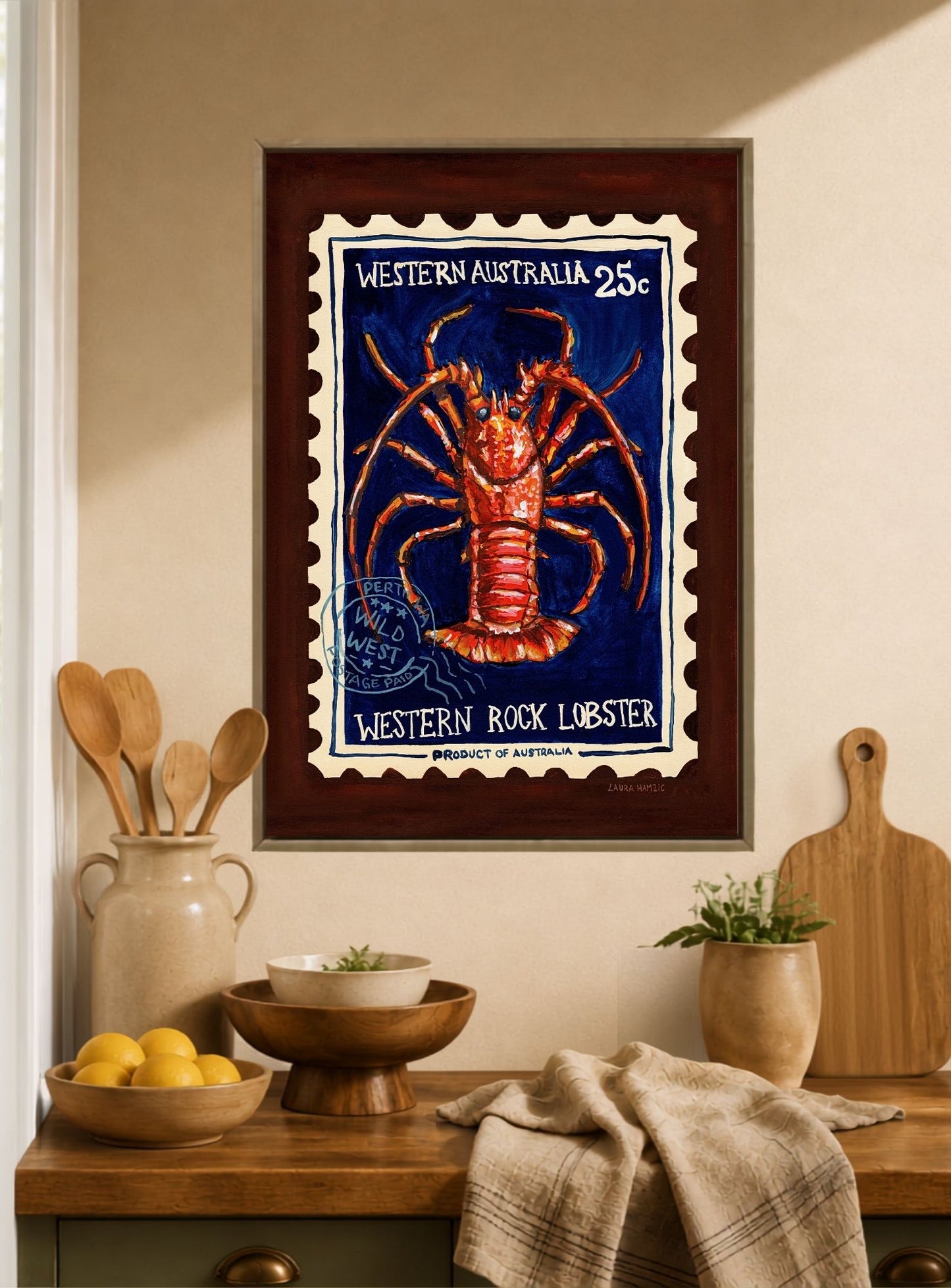 Framed wall art featuring a vintage-style stamp illustration of a red lobster on a dark blue background, with the text 'Western Australia 25c' and 'Western Rock Lobster,' displayed above a wooden countertop in a kitchen setting.