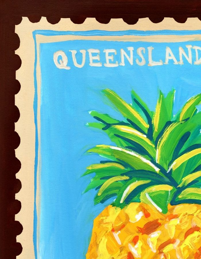 A close-up of a colorful painting or print featuring a pineapple with green leaves and a yellow-orange body, set against a bright blue background with the word 'QUEENSLAND' at the top. The artwork is shown with a scalloped border on a dark brown background.