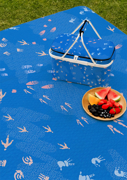 Blue picnic blanket and picnic featuring whimsical Australian wildlife footprints – kangaroo, echidna, wombat, and more – inspired by bushland trails and nature’s stories. Surface pattern design Australia.